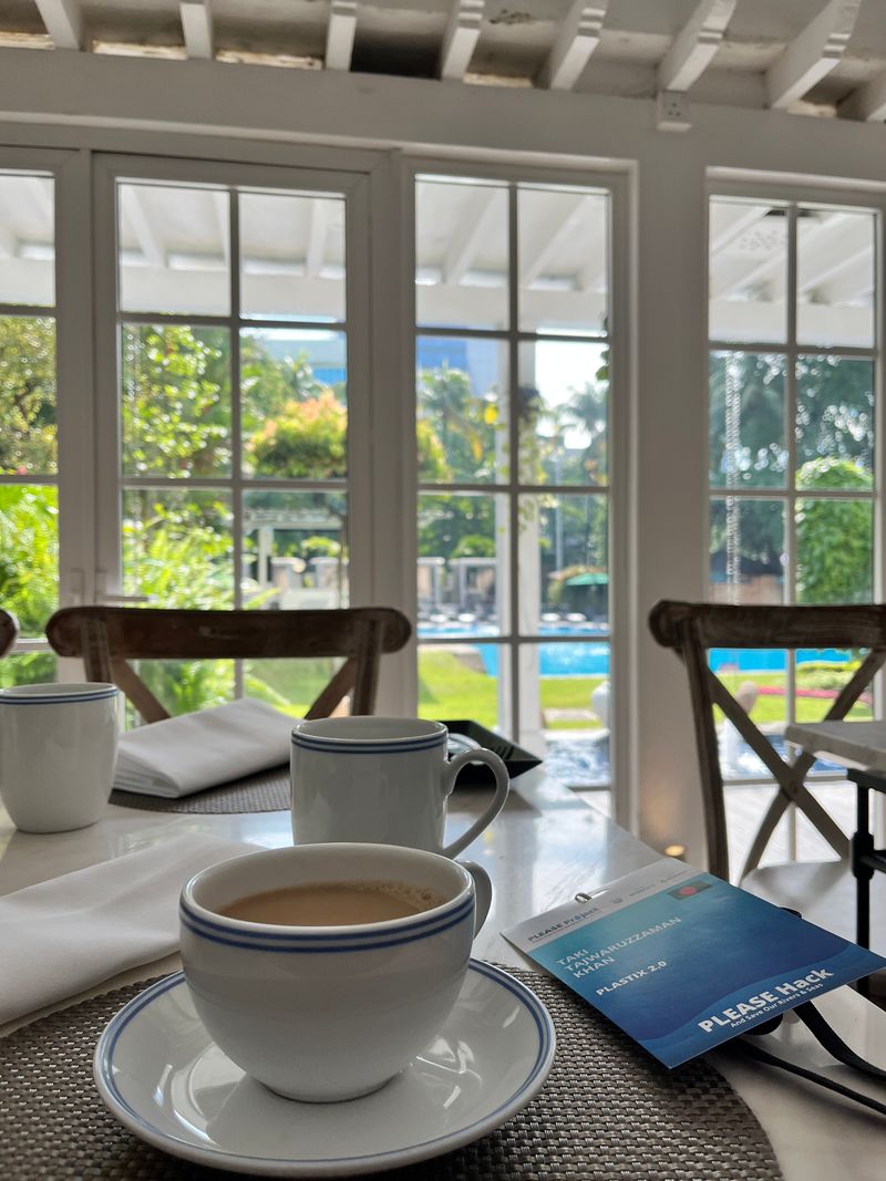 Coffee cups and a conference badge on a table overlooking a garden pool